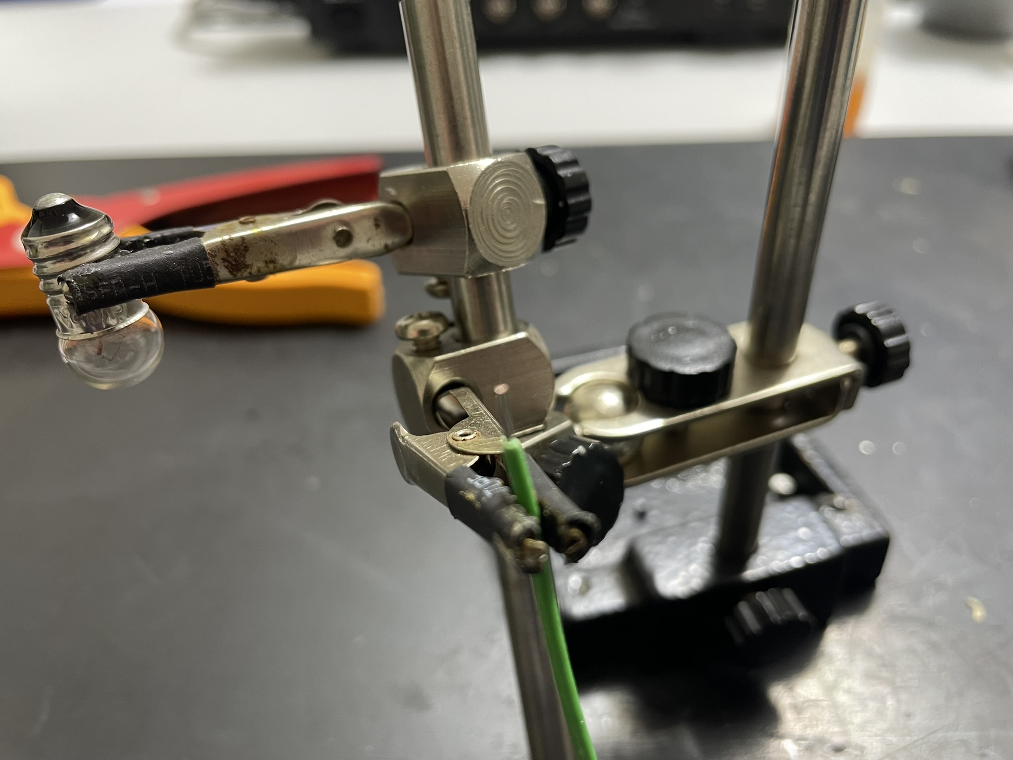 A mechanical device with various components on a test stand and mechanism, surrounded by wires and a background paper.