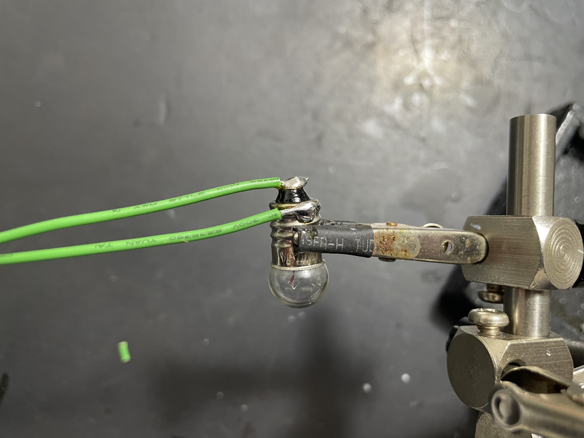 An electrical testing device with alligator clips, a metal cylinder, and a light bulb-like component for