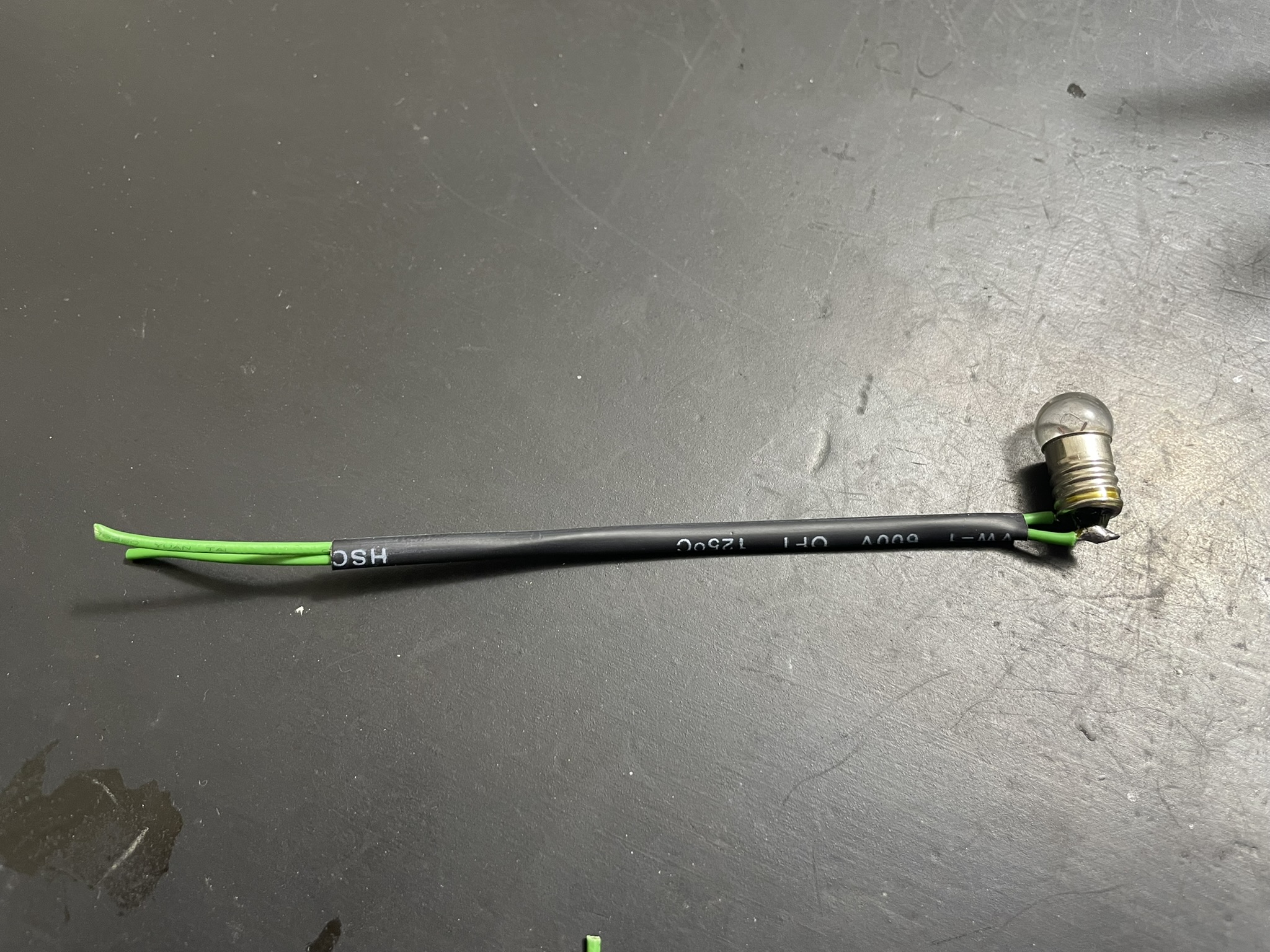 A black coiled wire with two ends, one attached to a plastic component, the other marked with green and white stripes.