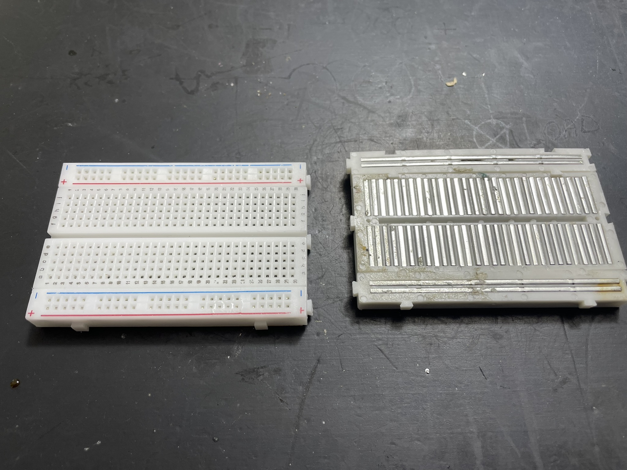 Two electronic boards with rows of metal pins, likely integrated circuits, on a breadboard with U-shaped strips for