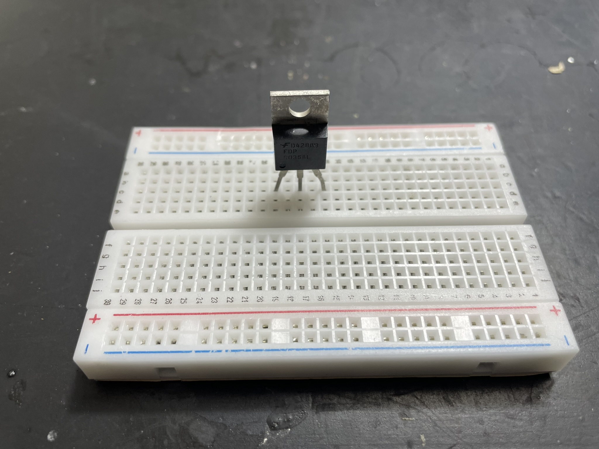 An electronic breadboard with jumper wire connected to GND pin, featuring a MOSFET and other components.