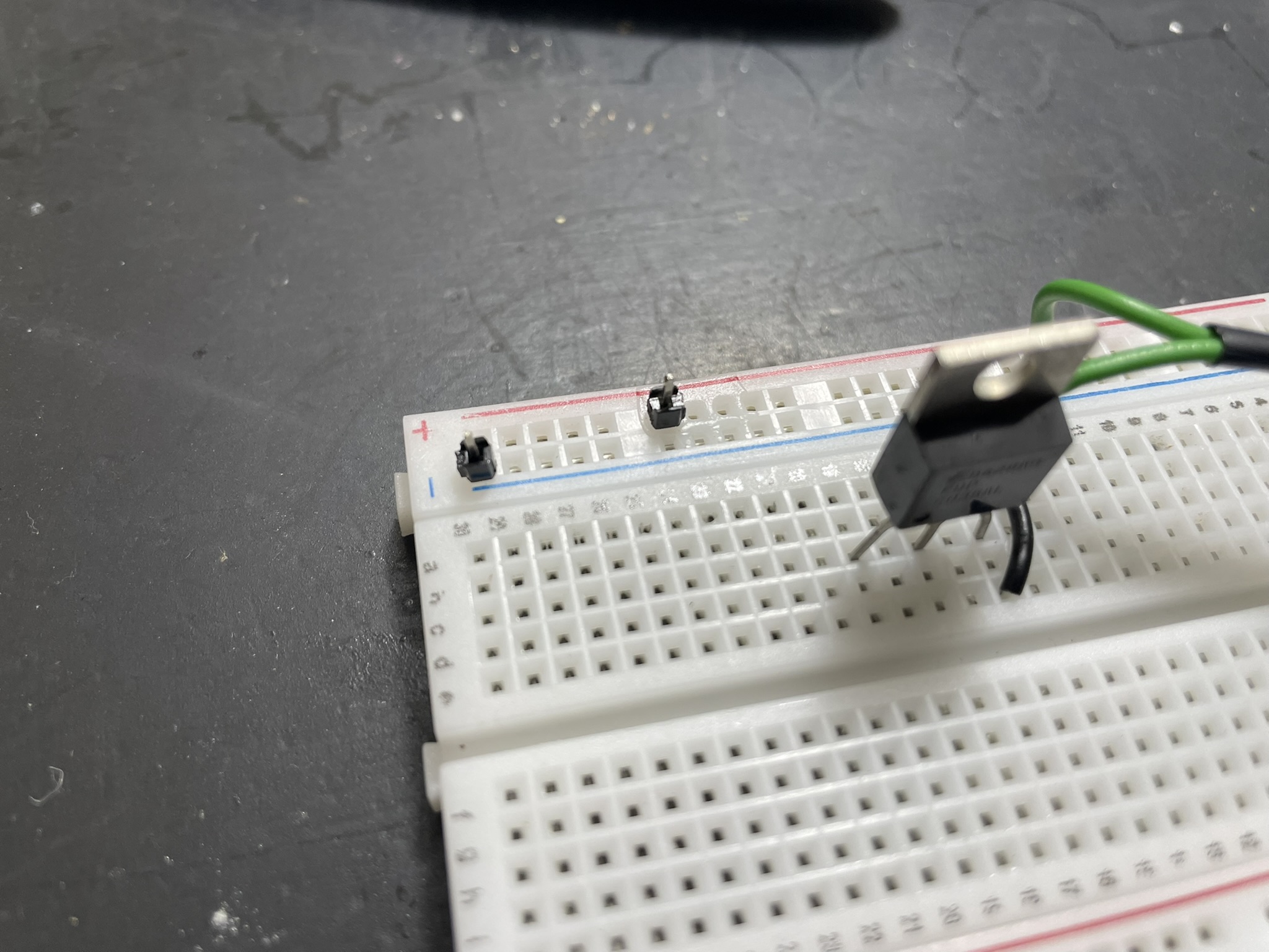 An electronic breadboard setup with a microcontroller and external power supply connected via header pins.