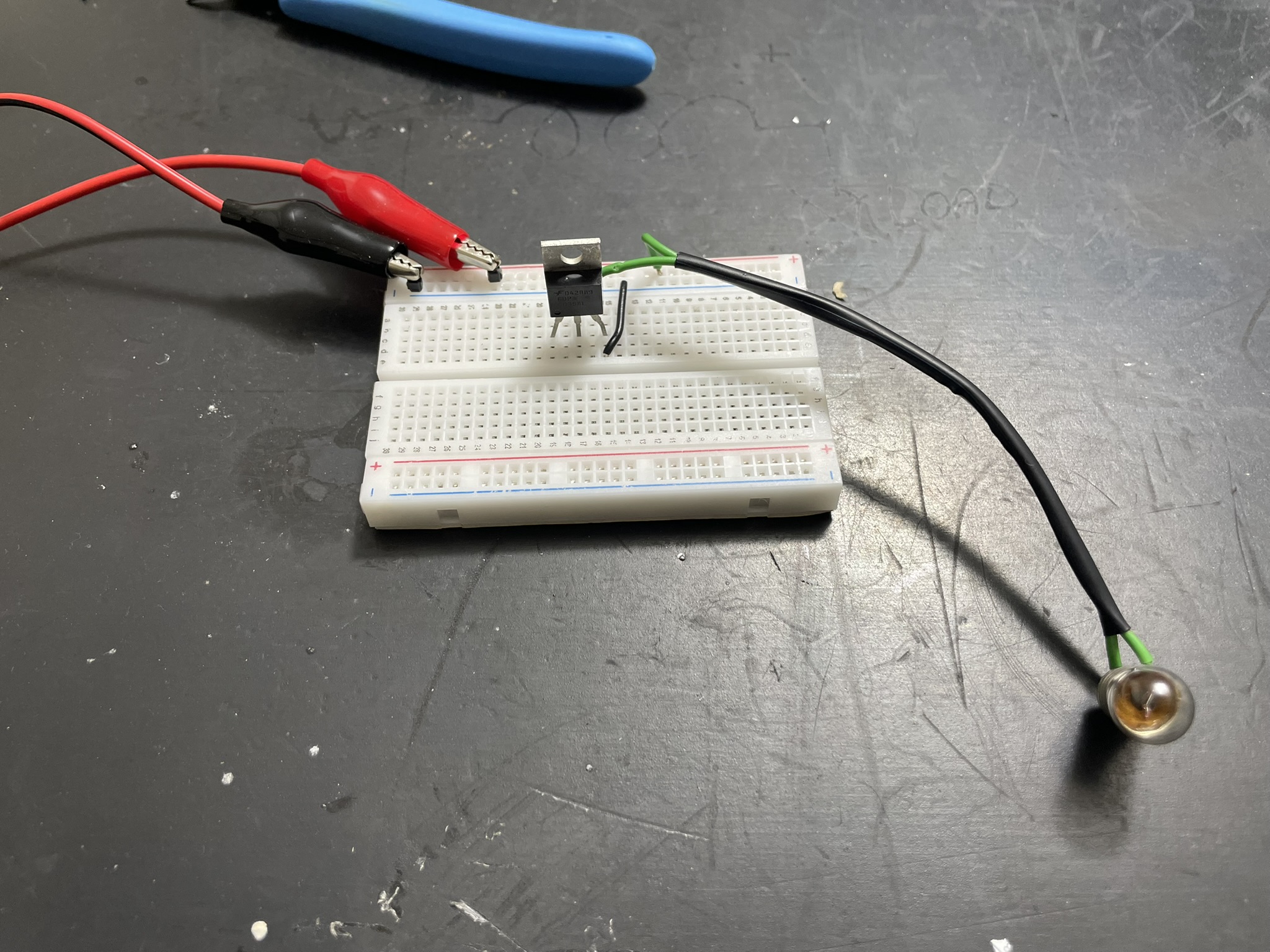 A breadboard with a circuit and LED lit up, connected to external power via header pins.