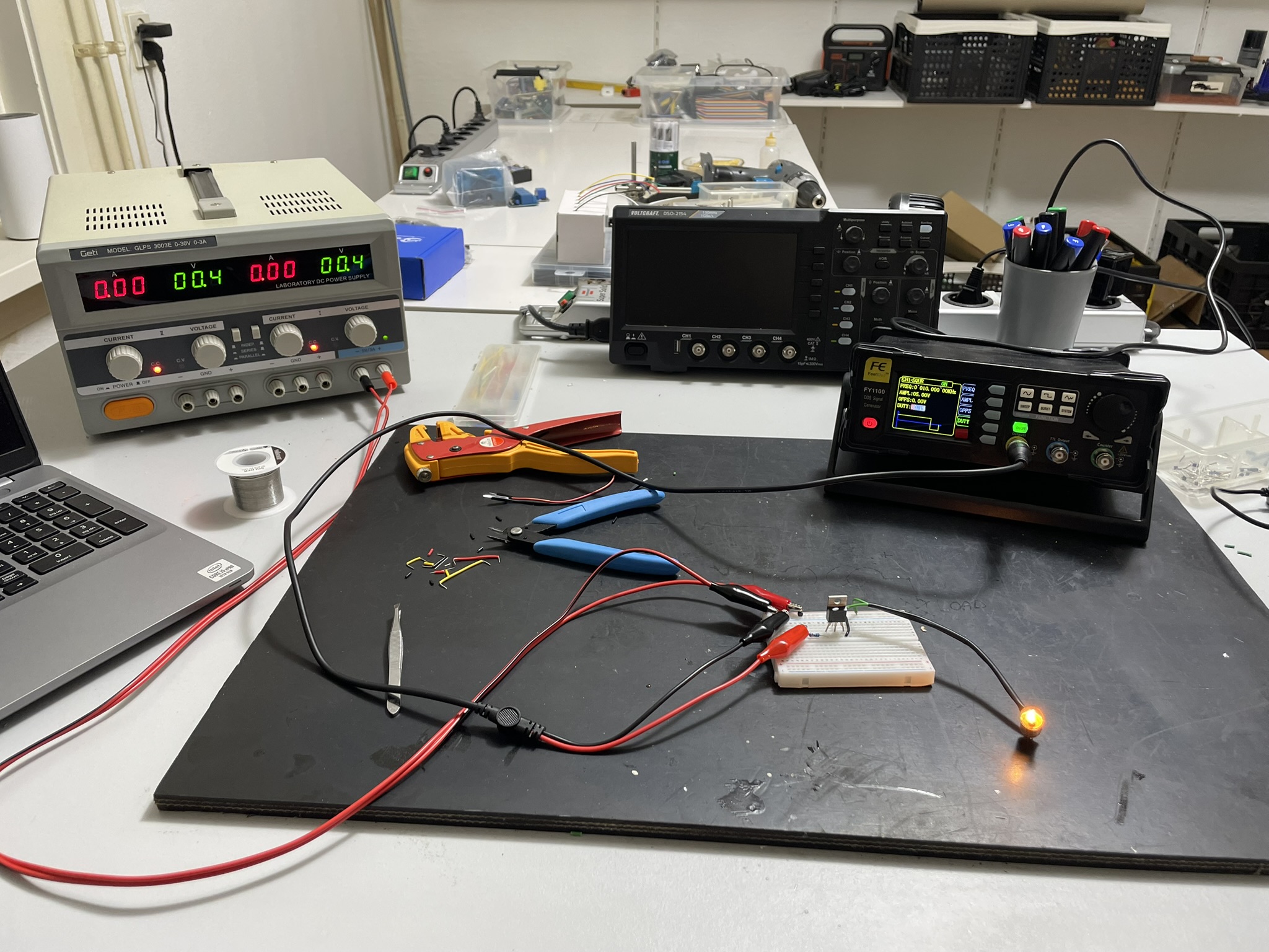 A laboratory setup with electronic equipment and components on a countertop, featuring an oscilloscope, multimeters,