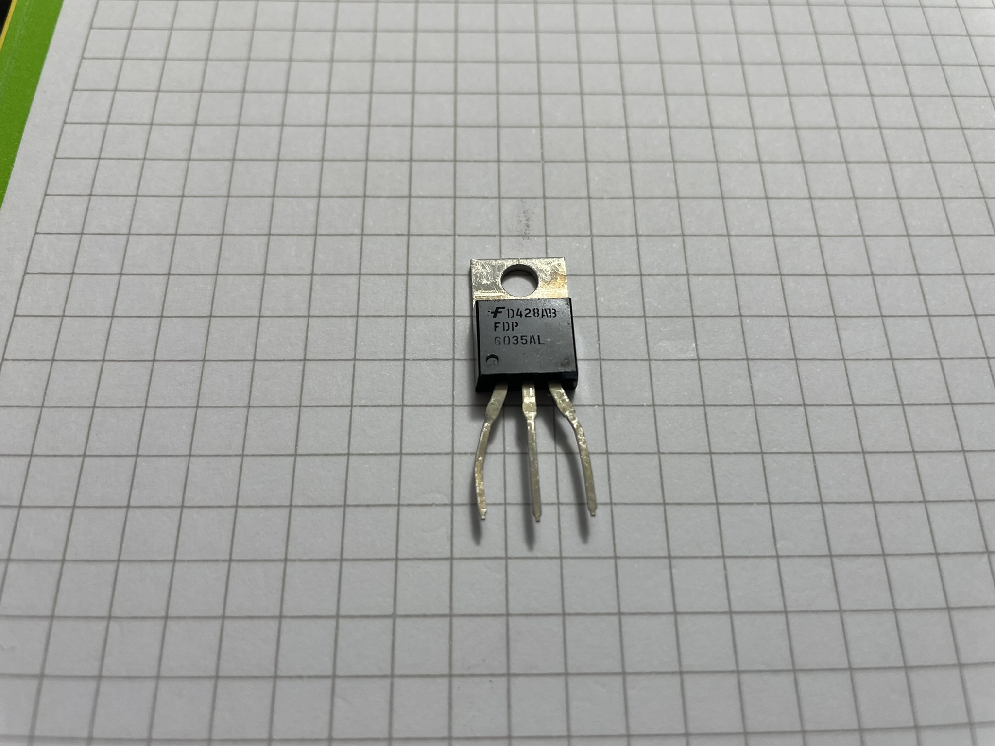 A small MOSFET IC with two legs soldered together, featuring pins on one end and etched text on its side.