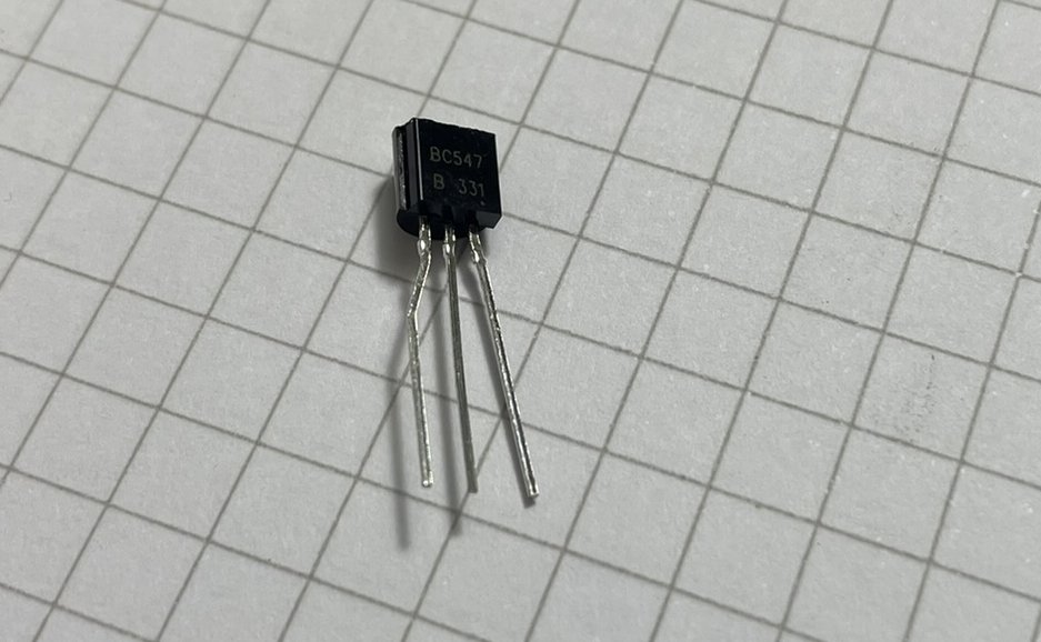 A small integrated circuit (IC) with multiple pins on a grid-patterned surface is shown.