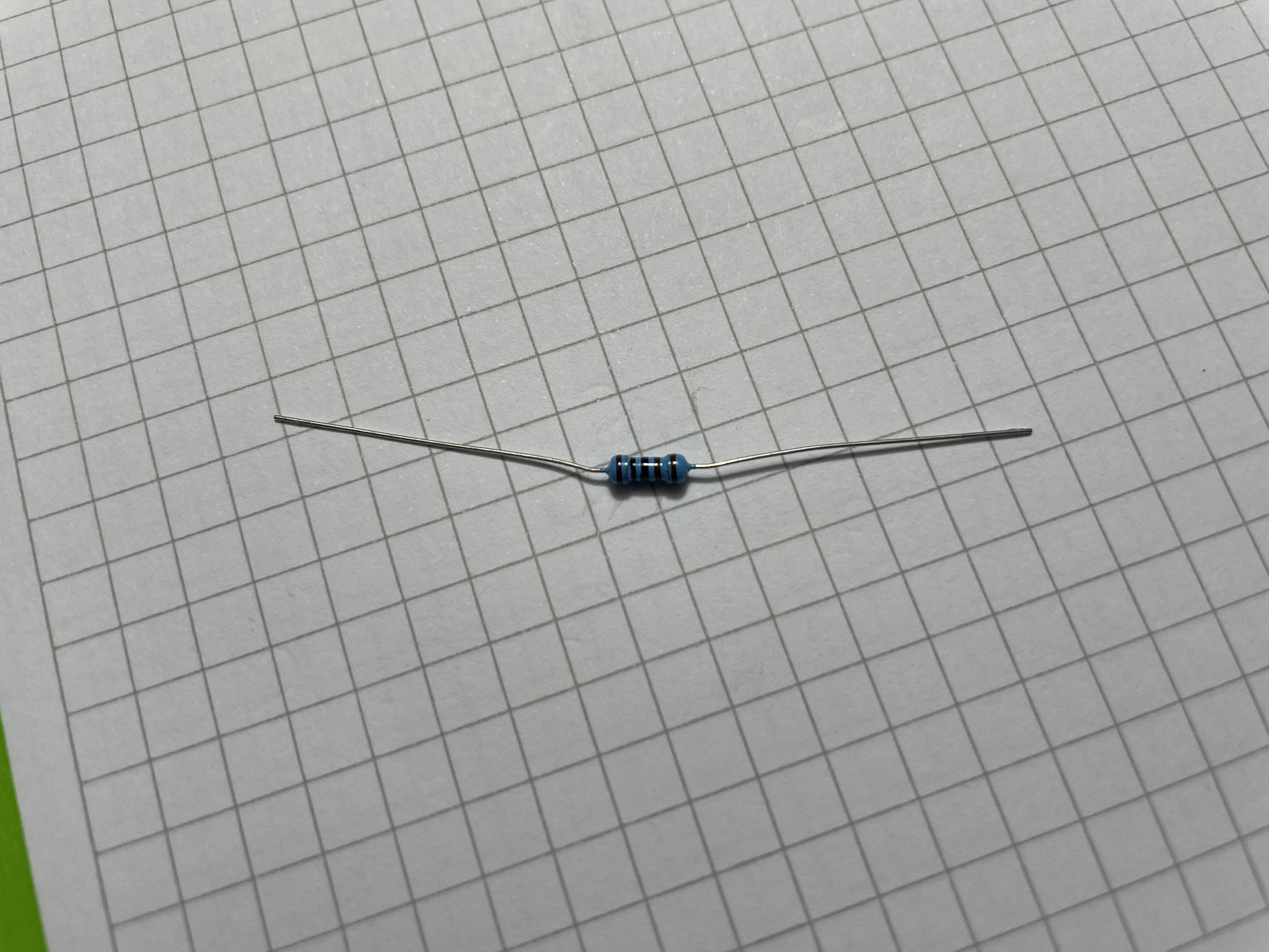 A small metal pin connector rests on grid-lined paper, with a flat top and bottom.