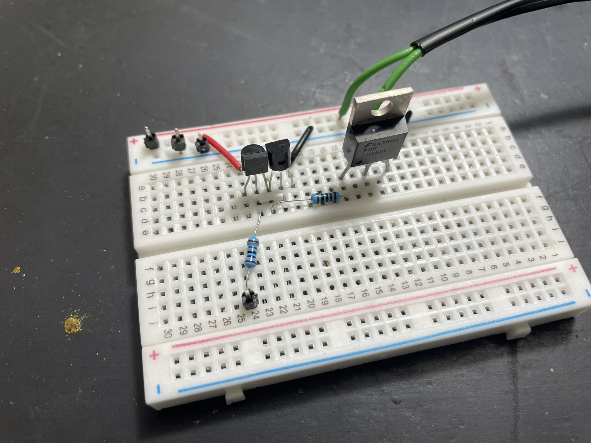 An electronics board with jumper wires, resistors, and capacitors surrounding an integrated circuit on a black surface.