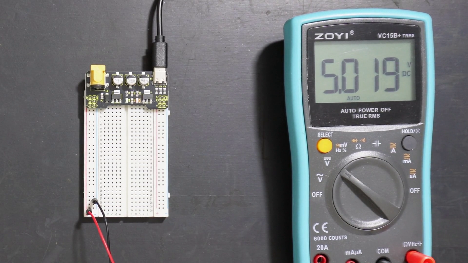 Breadboard power module with 5V left rail and 3.3V right rail, tested using banana-plug-to-crocodile-clip cables on a digital multimeter